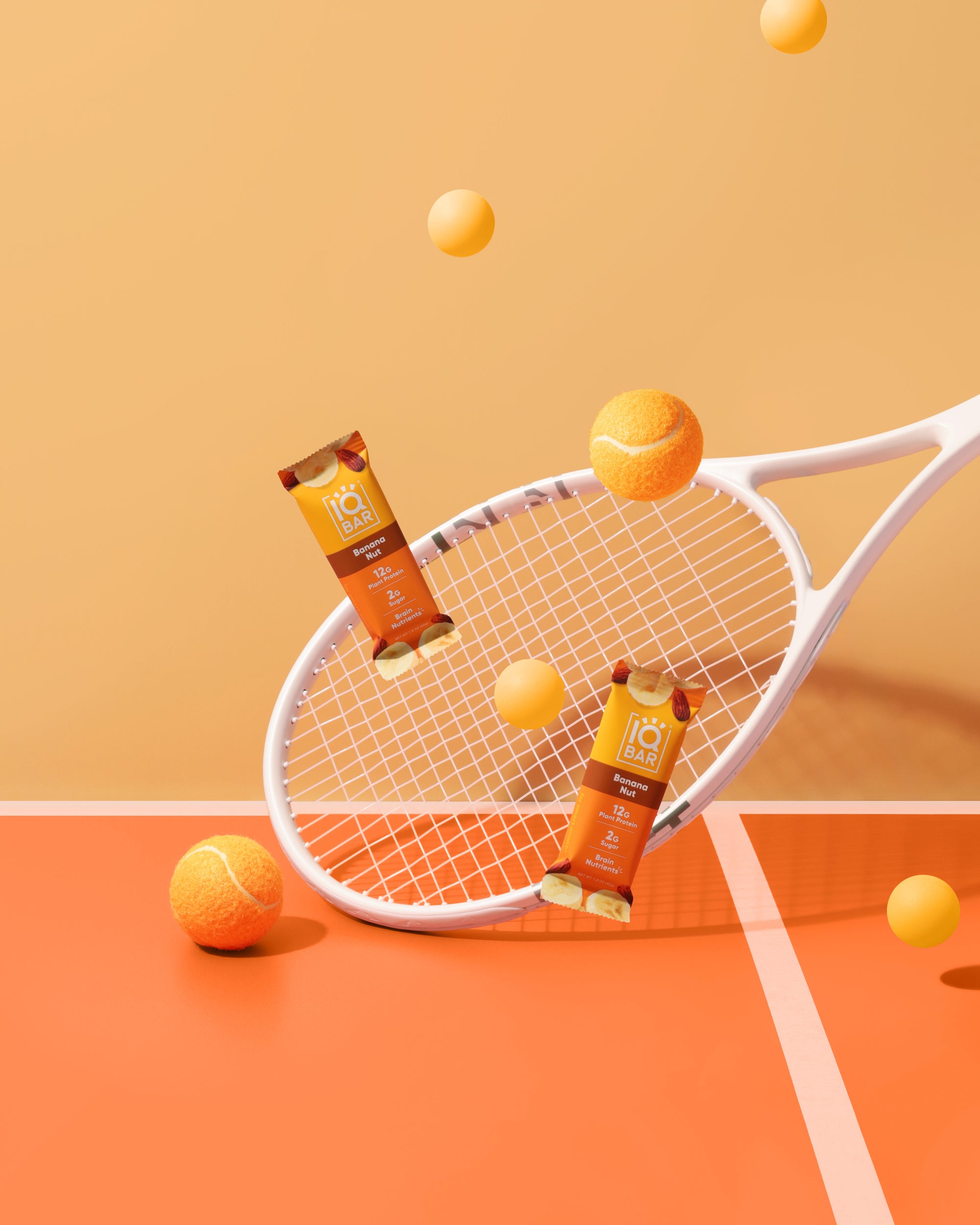 Tennis racket with tennis balls and Banana Nut IQBARs on an orange background